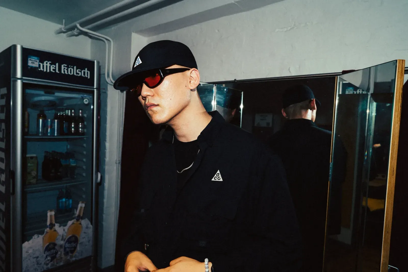 검은 모자와 선글라스를 쓰고 음료 냉장고 앞에 서 있는 DJ POOL