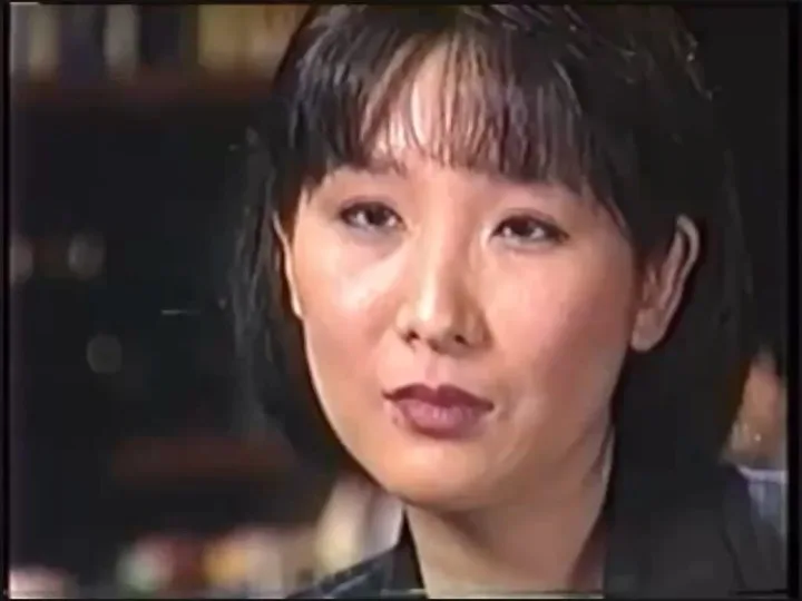 어두운 실내에서 카메라 옆을 보며 말하는 단발머리 여성. 인터뷰 영상의 한 장면