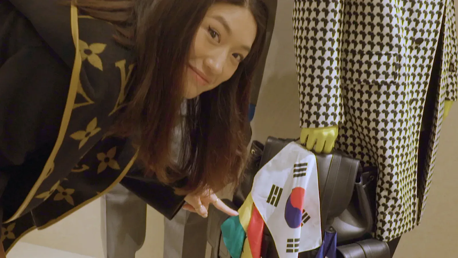 루이비통 모노그램 재킷을 입고 작은 태극기를 든 채 웃는 페기 구