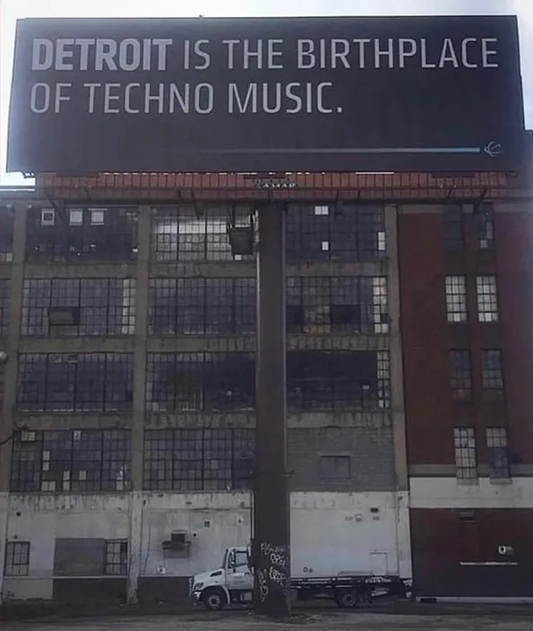 공장 건물 위에 걸린 검은 옥외 광고판. 「DETROIT IS THE BIRTHPLACE OF TECHNO MUSIC.」